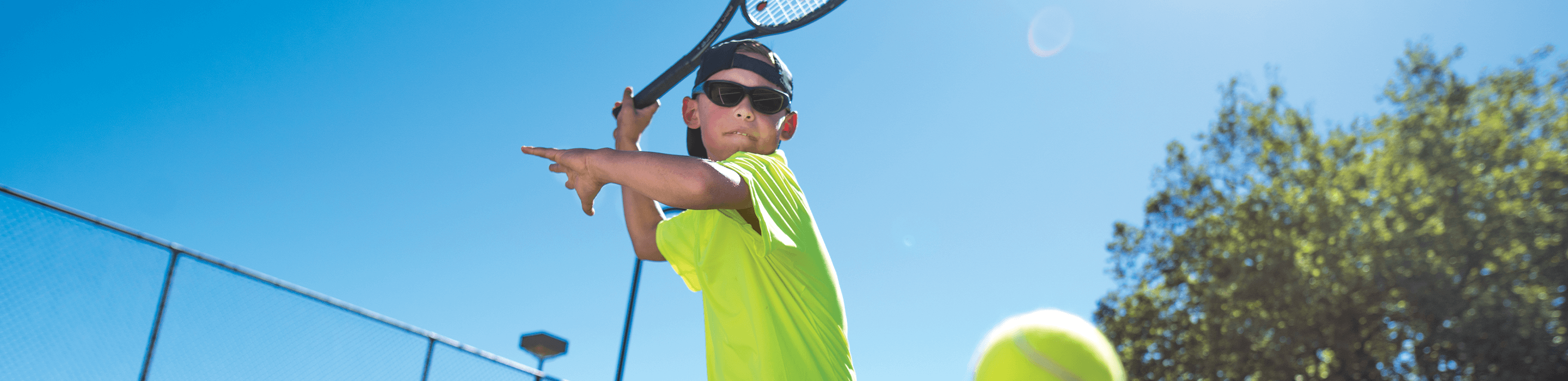 kid playing tennis and wearing sunglasses