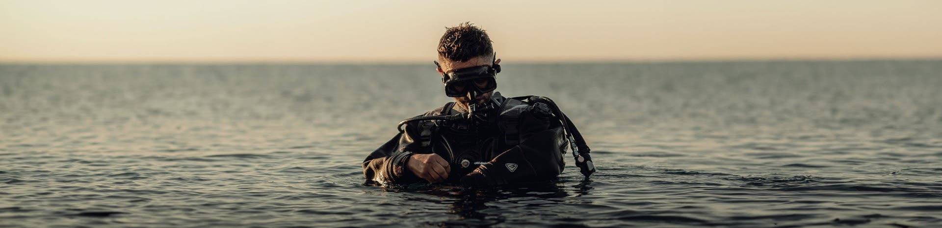 A man wearing a prescription scuba mask on his face while waist deep in the ocean