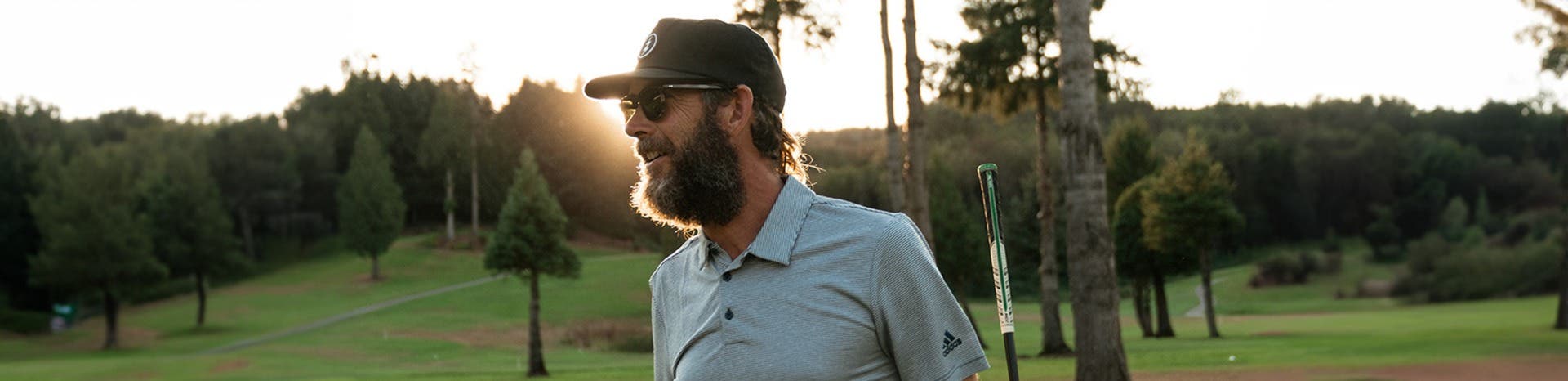 Side view of a smiling bearded man in prescription golf sunglasses at dusk.