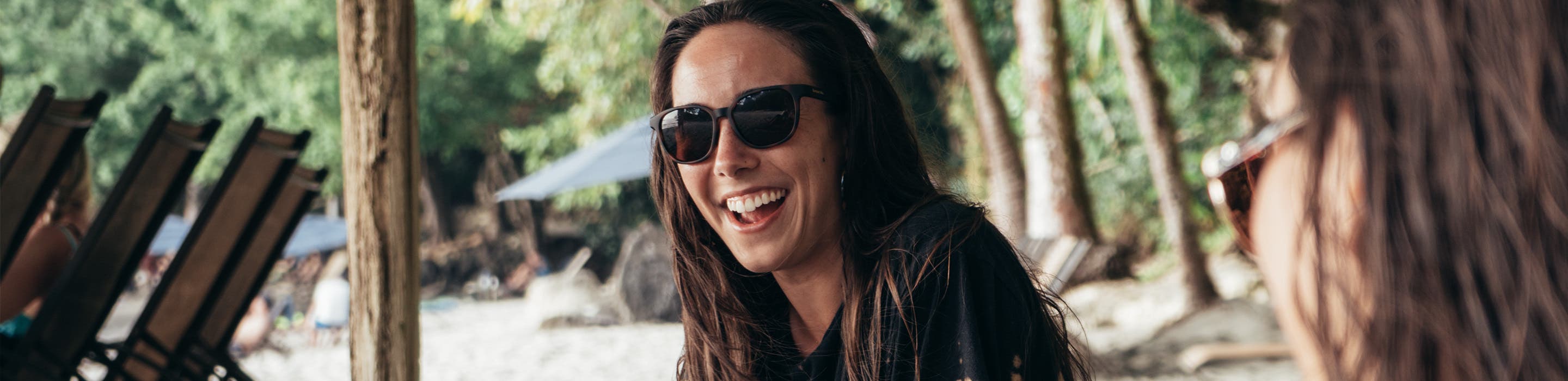 woman smiling and sitting on the beach wearing SportRx women's sunglasses