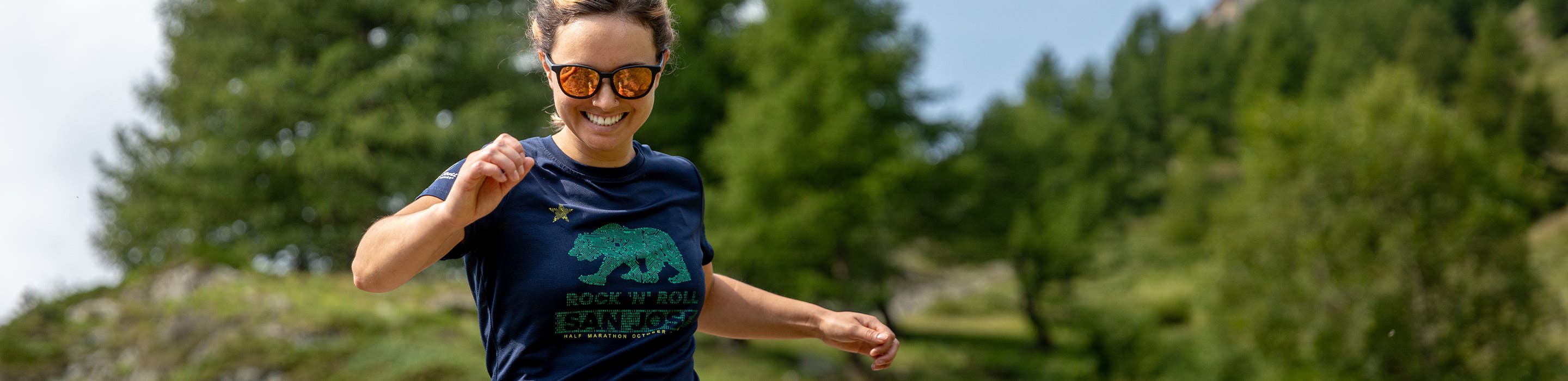 smiling woman running through the forest while wearing SportRx women's running sunglasses