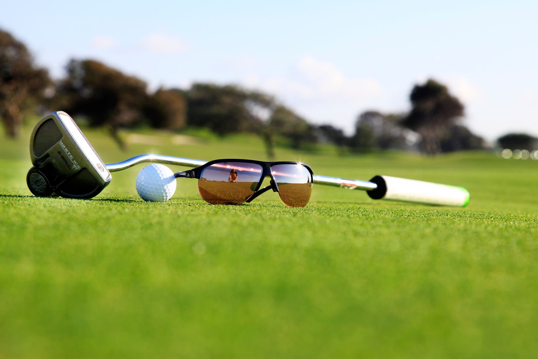 Golf course with club, sunglasses, and golf ball on ground.