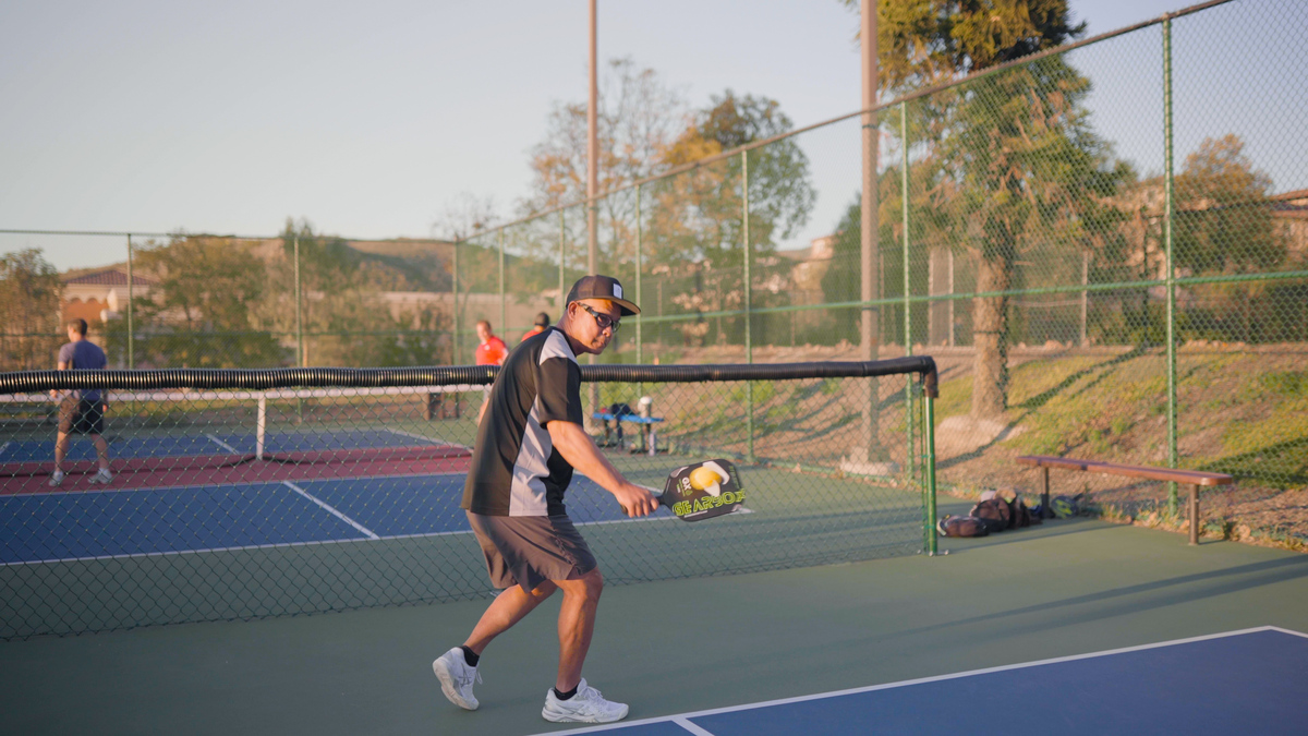 Man playing pickleball outside wearing eyewear.